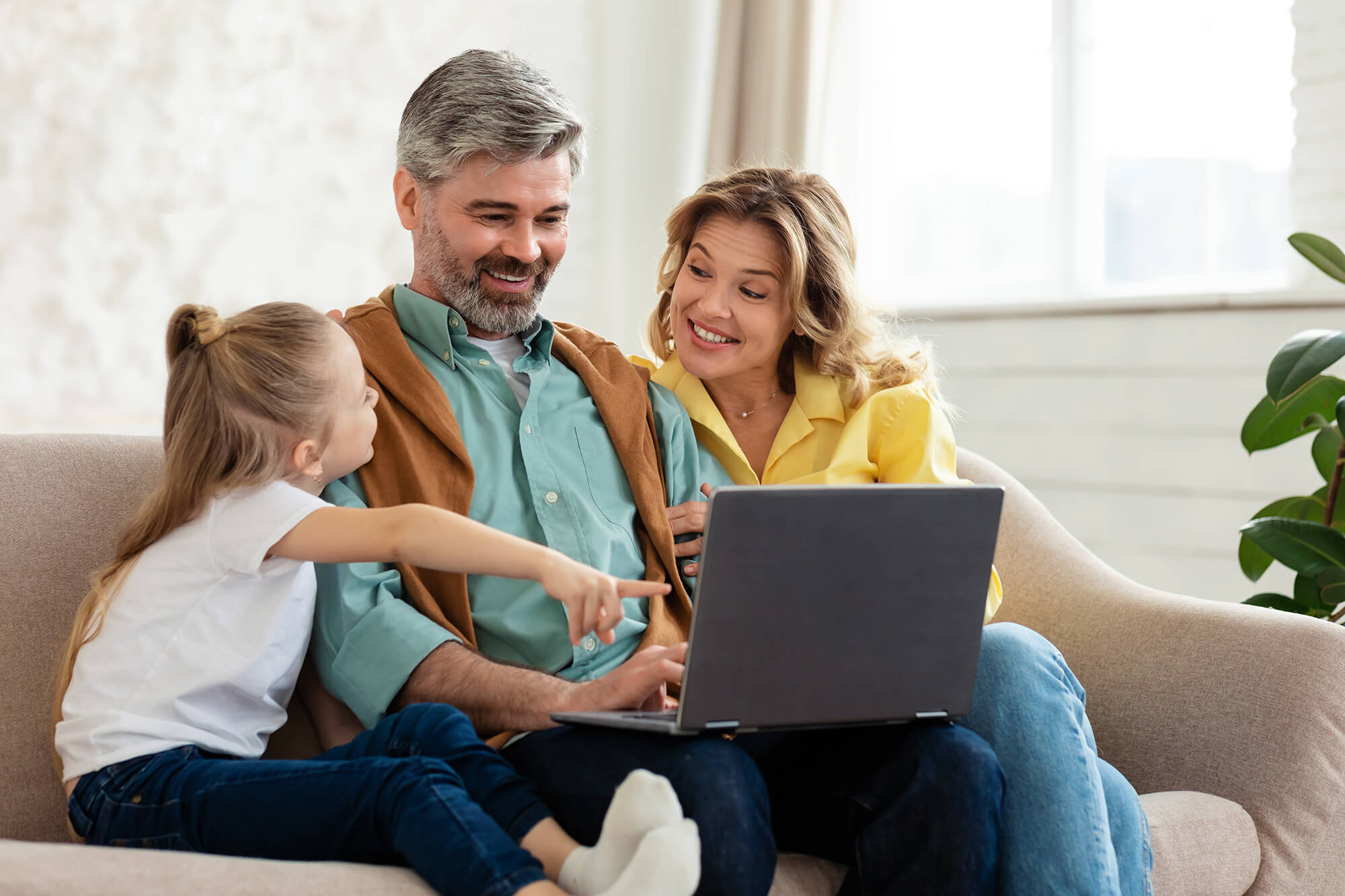 Family Of Three Using Laptop Computer Sitting On Sofa